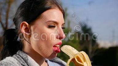 在阳光明媚的日子里，动作缓慢、身材迷人、有着美丽眼睛和红唇的年轻黑发女人吃香蕉